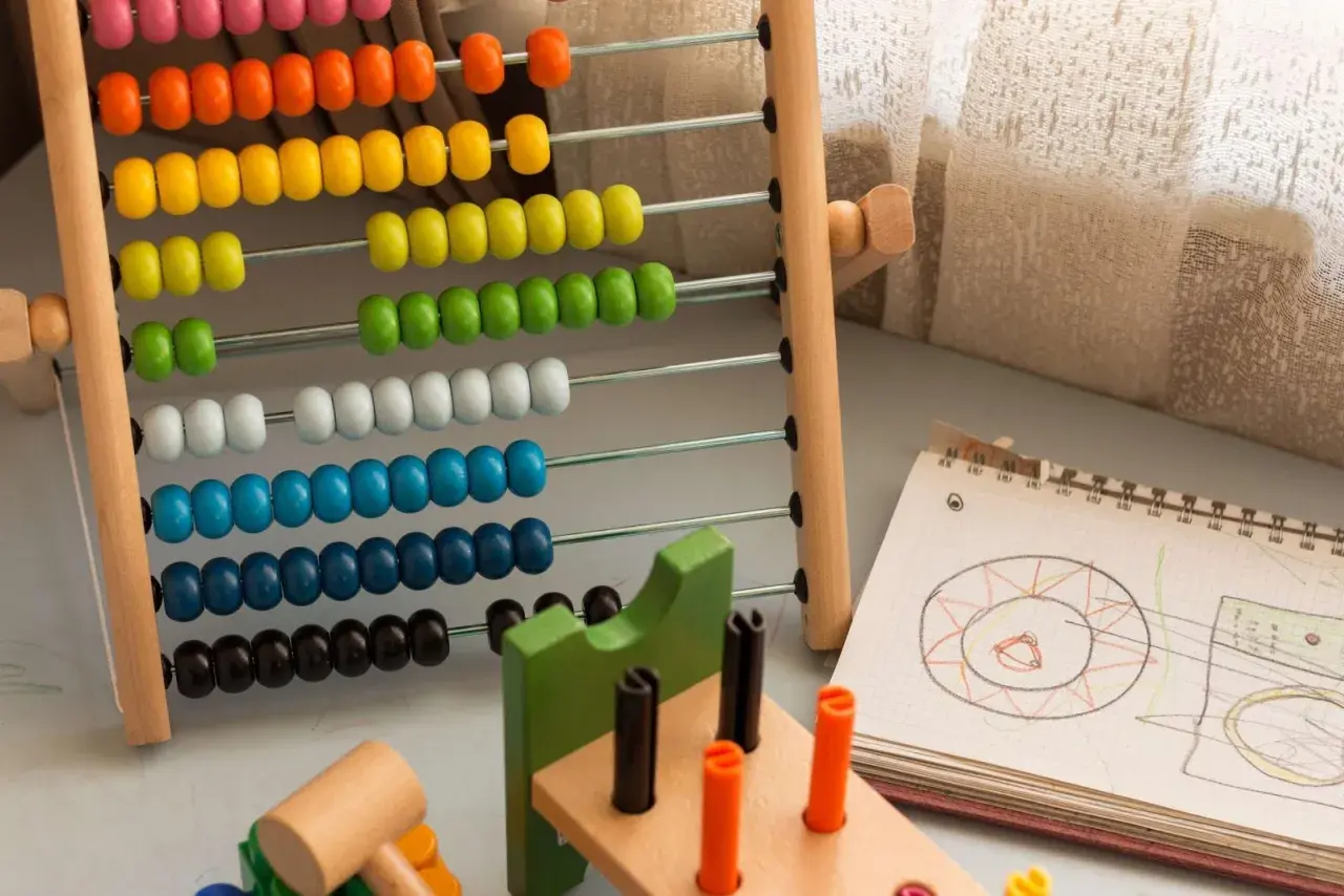 Ábaco de madera con cuentas de colores y un cuaderno con dibujos, ideales para ejercicios de atención y aprendizaje temprano.