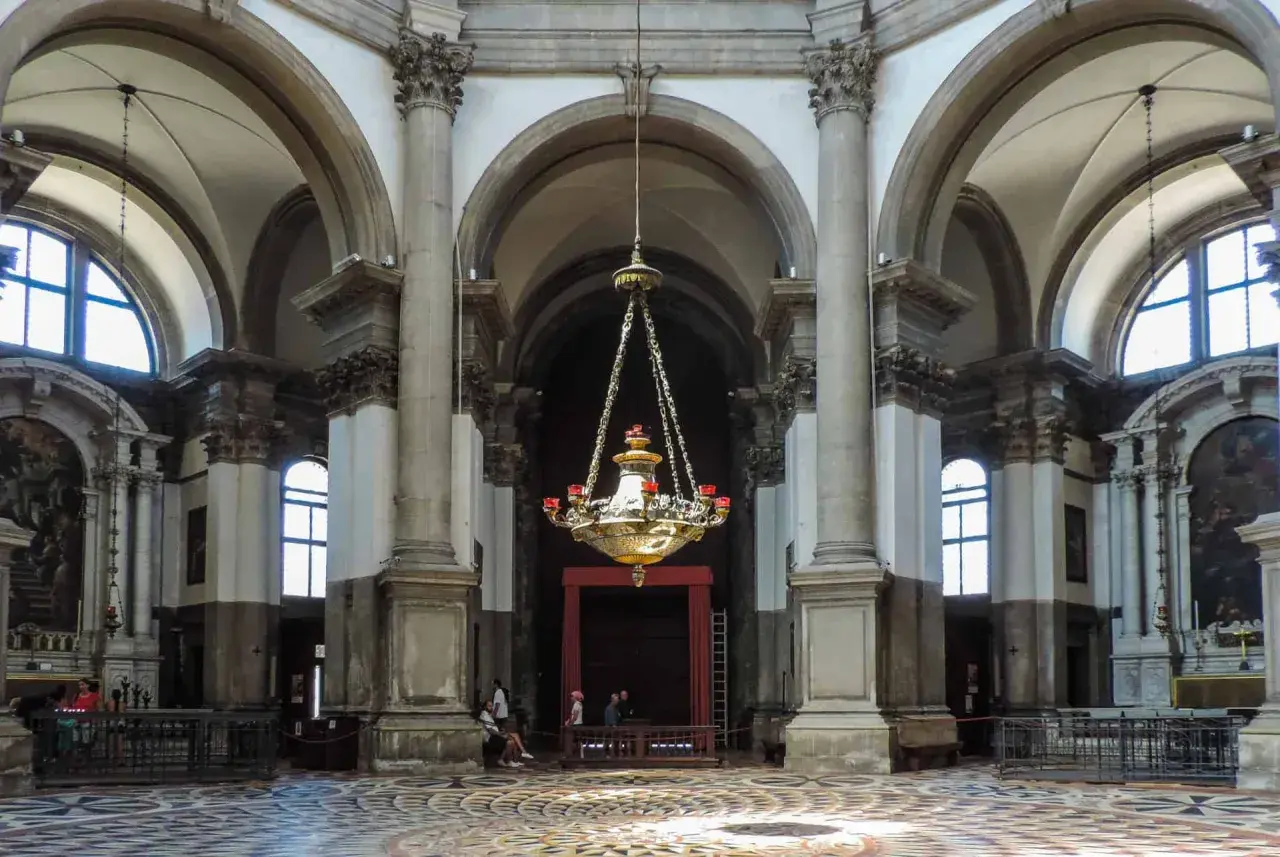 Intérieur de la basilique Santa Maria della Salute, avec son lustre imposant, ses colonnes majestueuses et son sol orné.