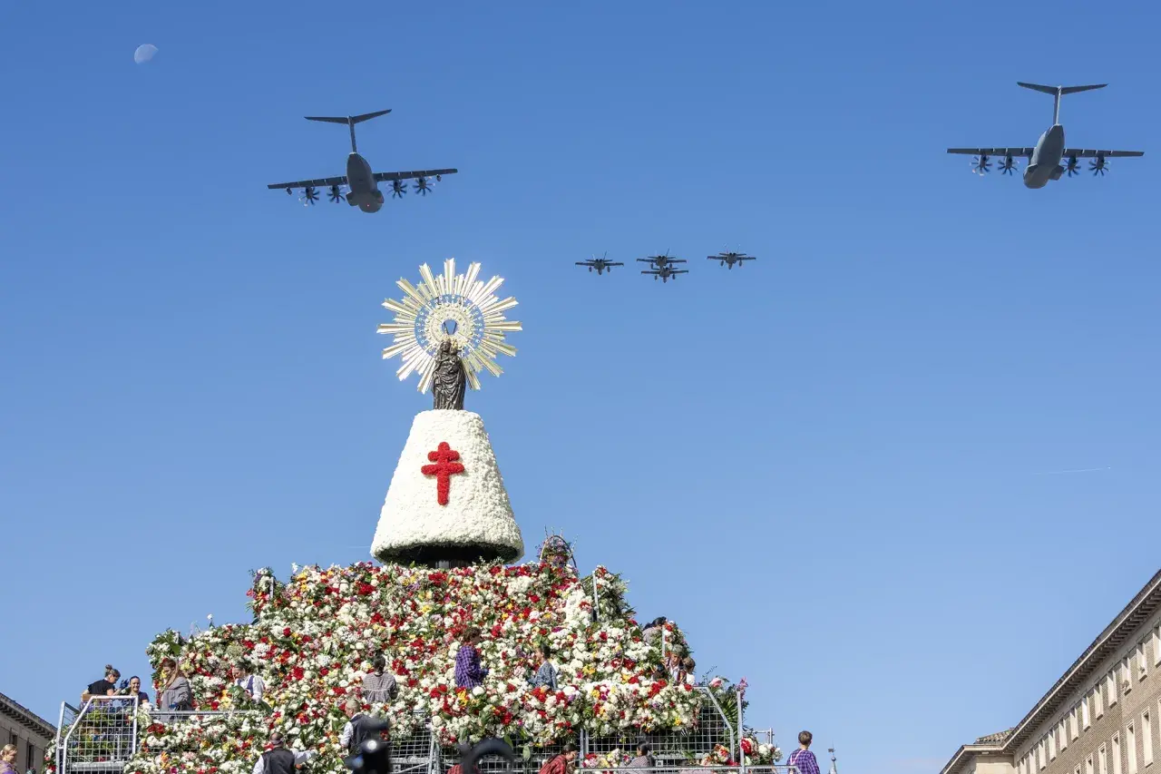 Desfile aéreo de aviones militares sobre una gran ofrenda floral y una imagen de la Virgen del Pilar, celebrando las fiestas del Pilar.