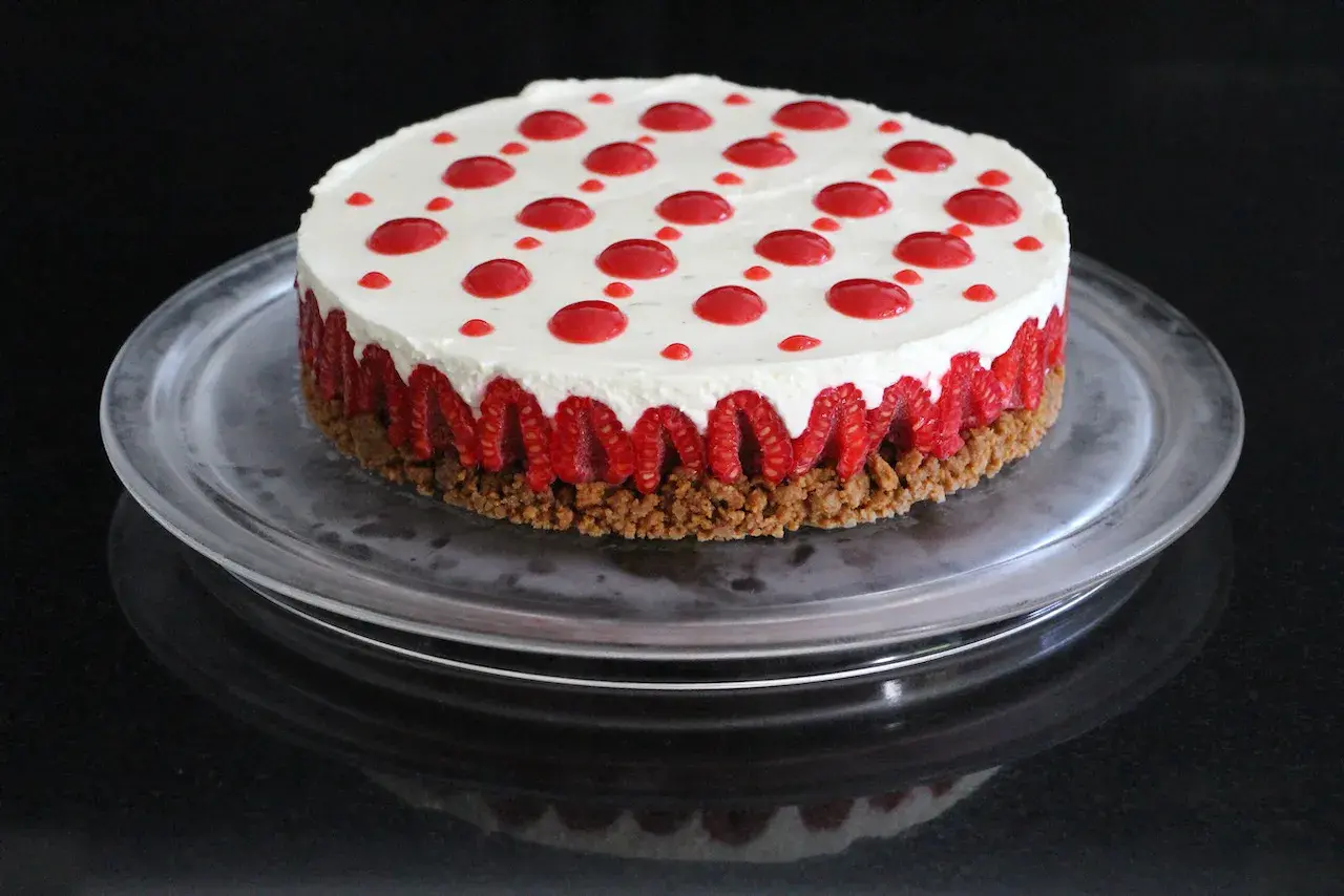 Cheesecake sans cuisson aux framboises, garni de points de coulis rouge sur une base croustillante.