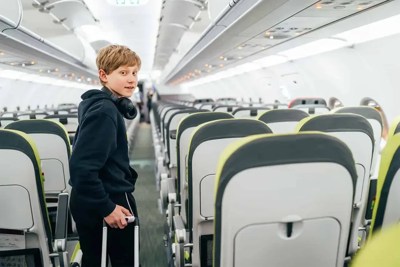 Chłopiec z walizką i słuchawkami na szyi w samolocie. Wizzair od ilu lat można latać samemu?
