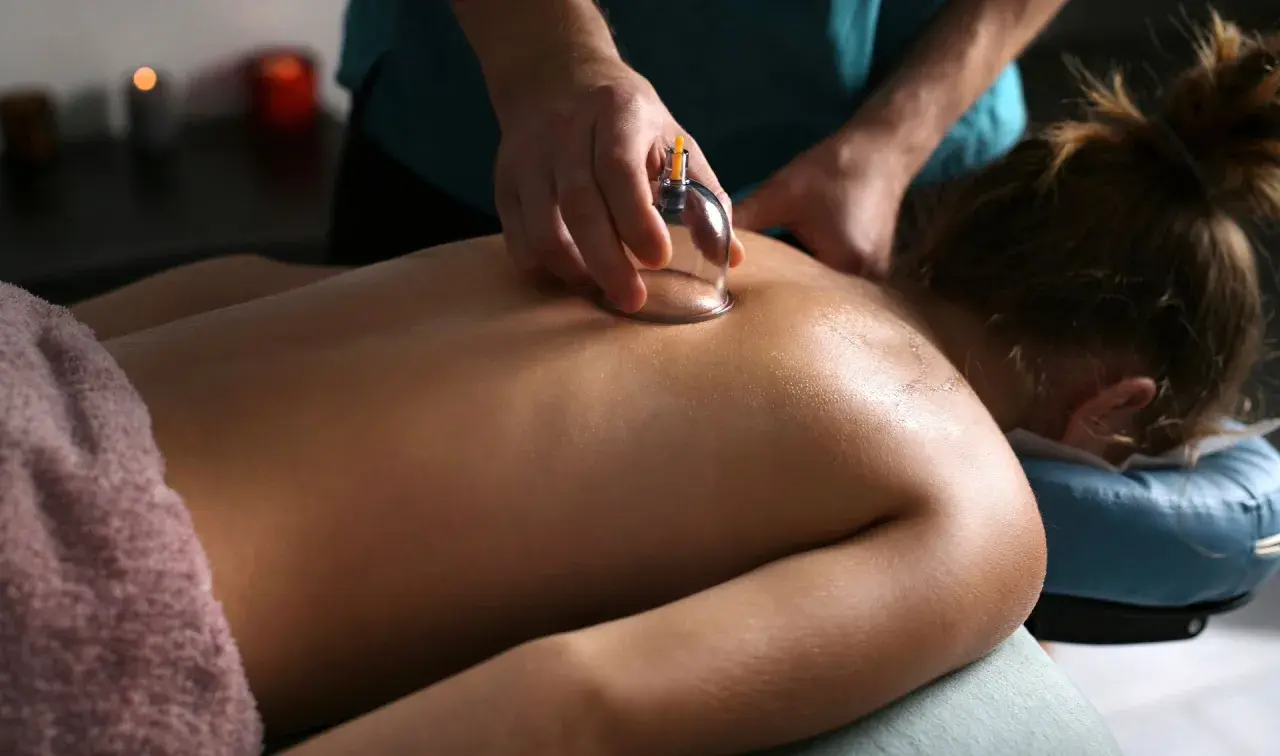 Un praticien applique une ventouse pour un drainage lymphatique du dos. La peau est huilée, créant un effet lumineux.