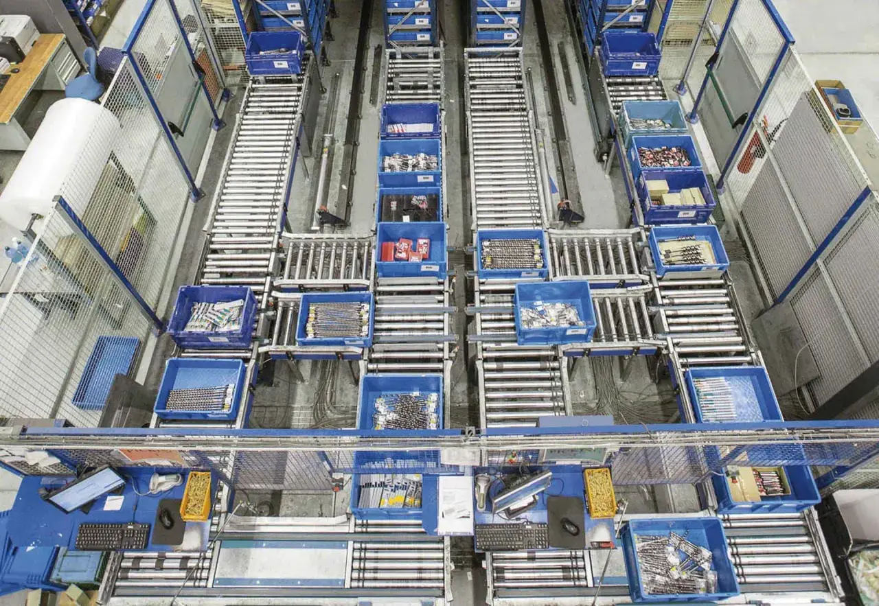 Ein Lager mit Rollenbahnen und blauen Behältern, die Werkzeuge und Materialien enthalten. Dies zeigt die Effizienz und Organisation, die durch Kanban-Vorteile erreicht werden.