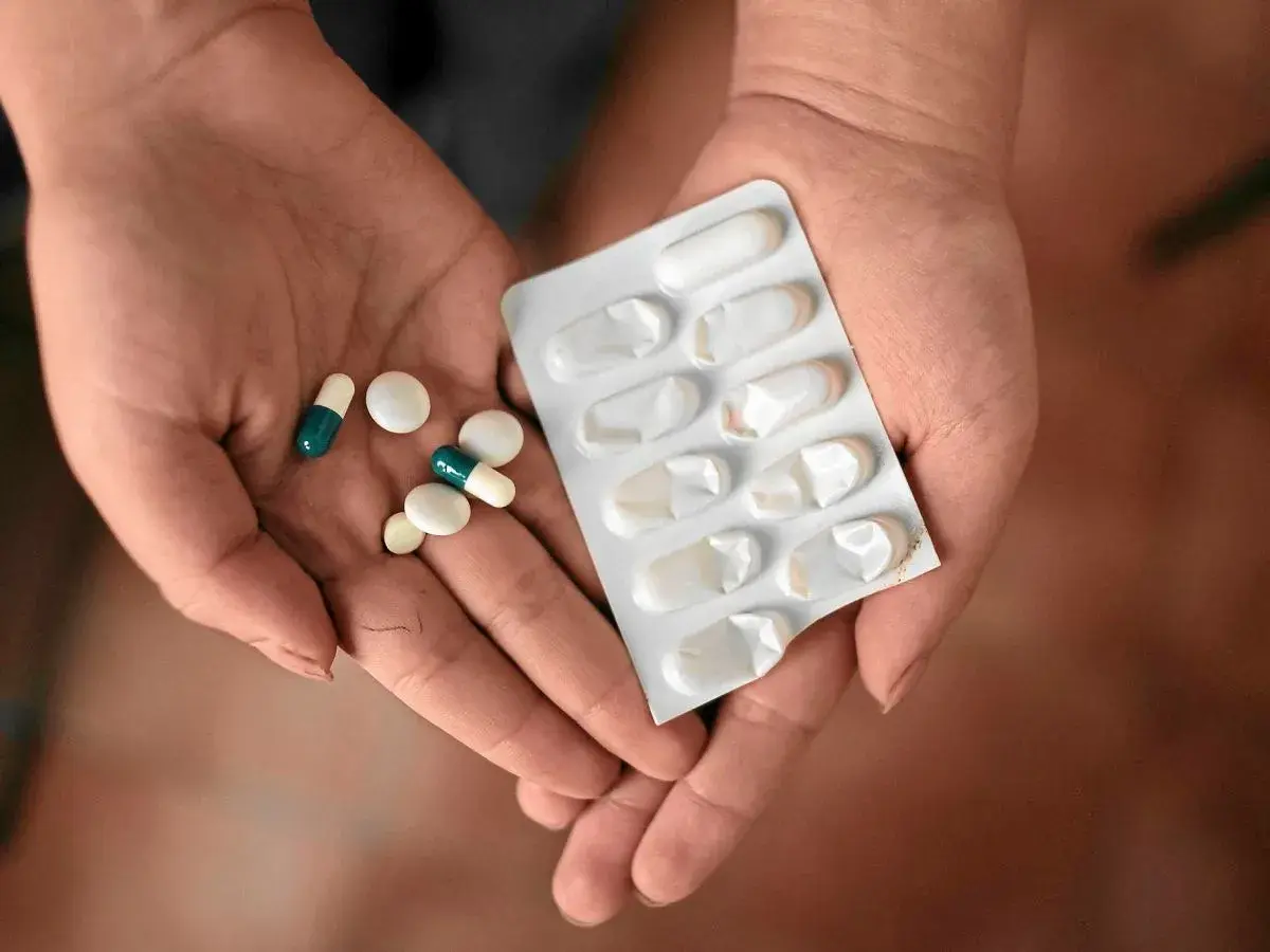 Dłonie trzymające tabletki i blister. Jedna z nich zawiera leki, które mogą być **inhibitory pompy protonowej**, stosowane w leczeniu problemów żołądkowych.