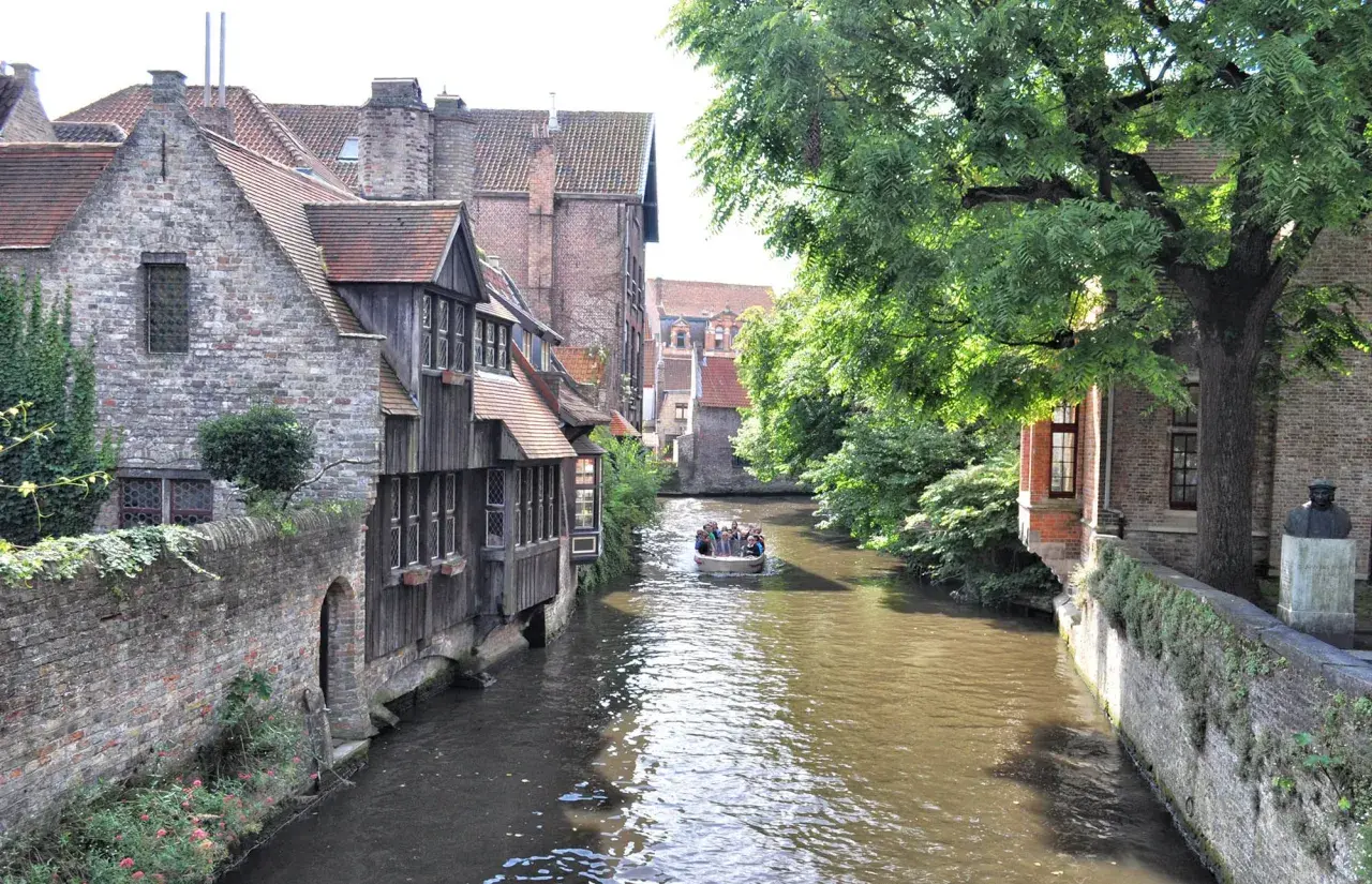 Un paseo en barco por los canales es ideal para ver Brujas en un día. Casas antiguas y árboles frondosos bordean el agua.