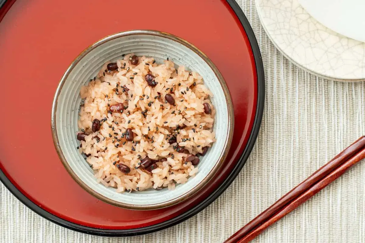 A bowl of Japanese red bean rice, sprinkled with black sesame seeds, sits on a red tray.