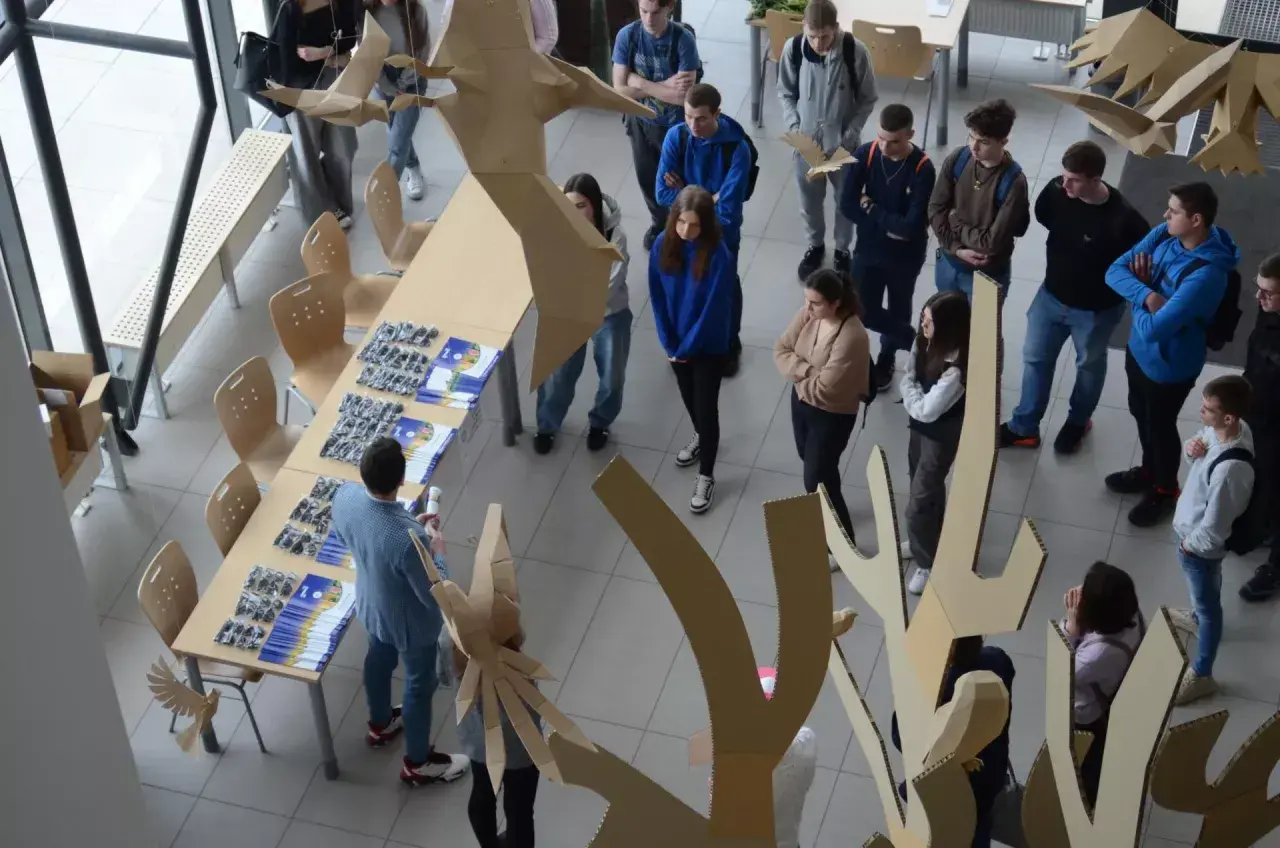 Studenci podczas prezentacji projektów z dziedziny studiów rolniczych, otoczeni kartonowymi instalacjami.