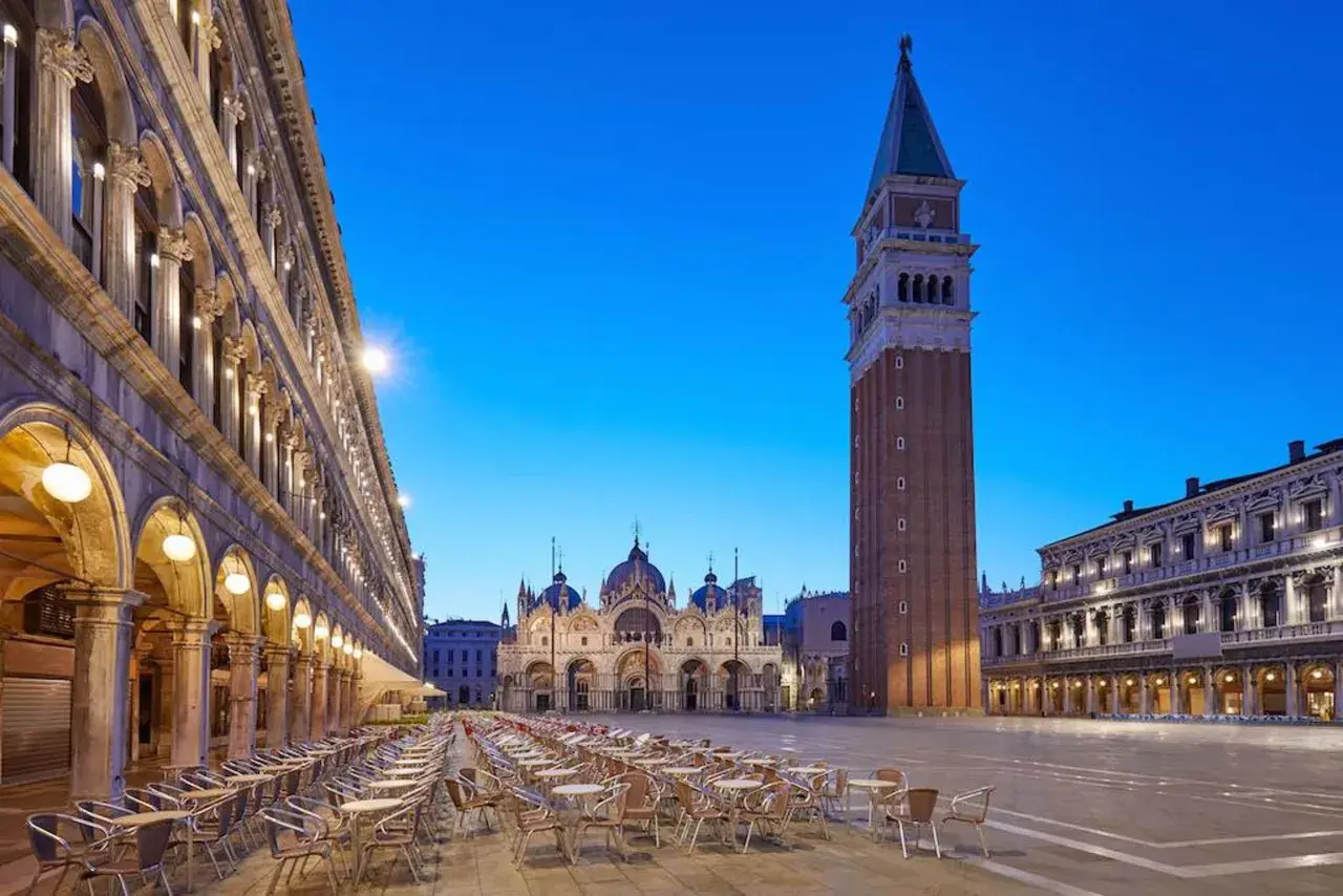 Un maestoso palazzo in Piazza San Marco, Venezia, si erge con la sua architettura imponente, mentre il cielo azzurro della sera fa da sfondo.
