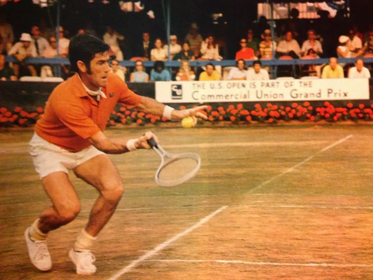 Ken Rosewall w akcji na korcie, w pomarańczowej koszulce i białych spodenkach, podczas meczu U.S. Open.