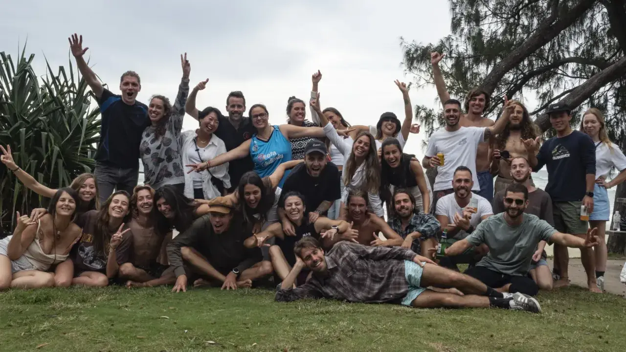 Grupo de jóvenes sonriendo y saludando, celebrando su **gap year** en la playa.