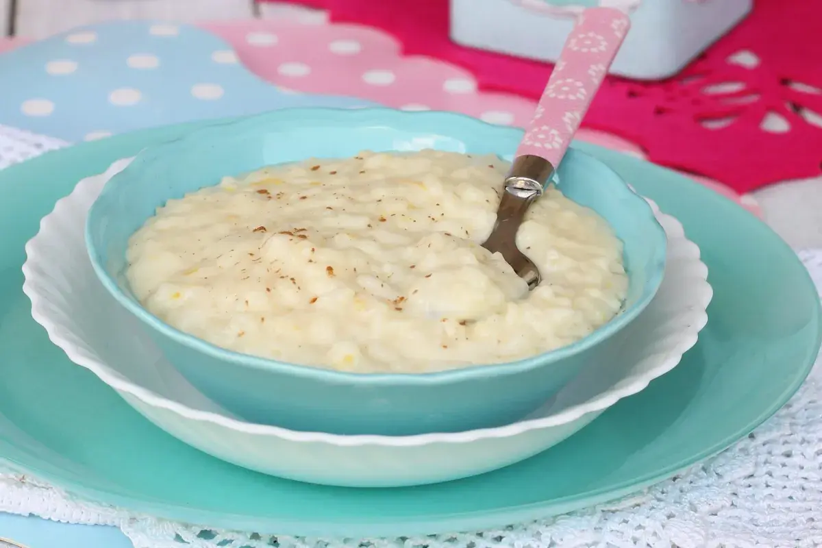 Un cremoso riso e latte, cosparso di cannella, servito in una ciotola azzurra con un cucchiaino rosa.