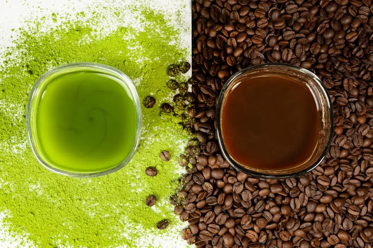 Zielony napój matcha obok ciemnej kawy, otoczone proszkiem matcha i ziarnami kawy. Wybór na poranek: matcha zamiast kawy?