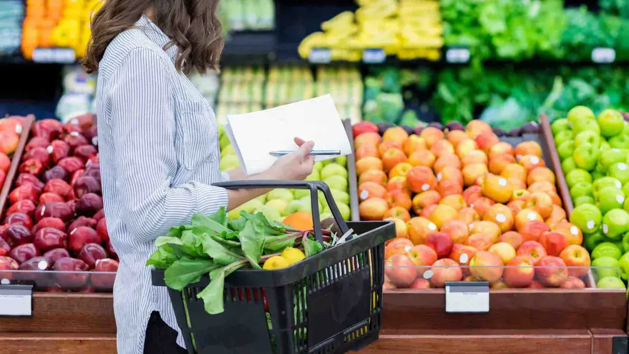 Donna con lista della spesa sceglie verdure fresche e frutta colorata al supermercato.