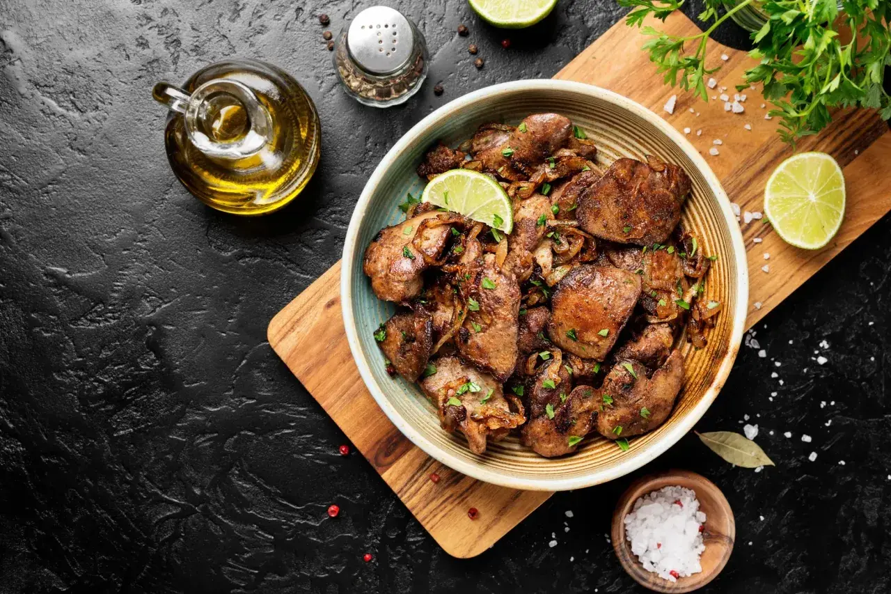 Un piatto invitante di fegatini di pollo con patate, guarnito con spicchi di lime e prezzemolo fresco. Accanto, olio d'oliva, sale grosso e pepe.