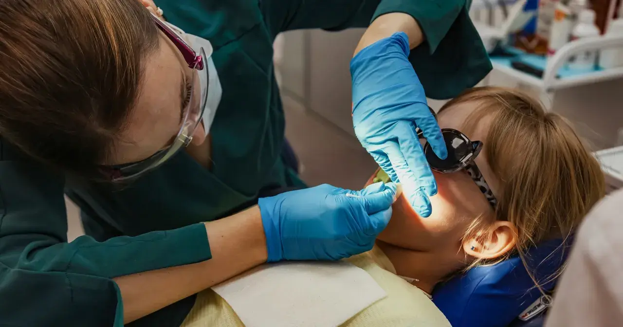 Dentystka wykonuje lakowanie zębów u dziecka. Sprawdź, jaka jest lakowanie zębów cena i zadbaj o uśmiech swojej pociechy.