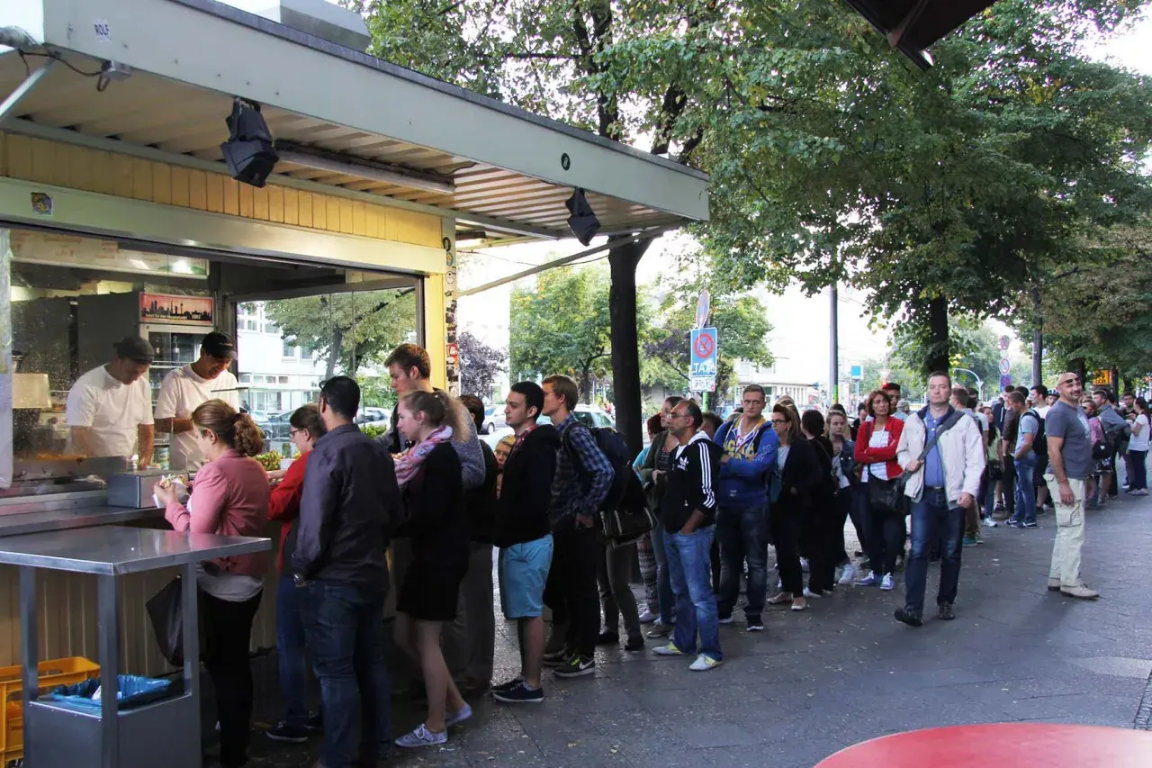 Długa kolejka do popularnego stoiska z kebabem w Berlinie. Ludzie cierpliwie czekają na swoje zamówienie, ciesząc się atmosferą miasta.