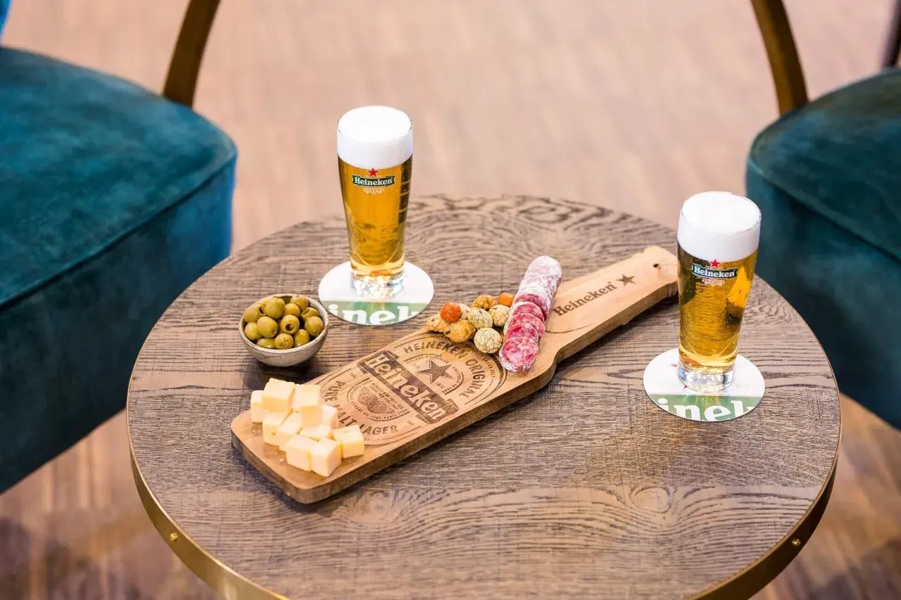 Due bicchieri di birra ale Heineken con salumi, formaggio e olive su un tavolino di legno.