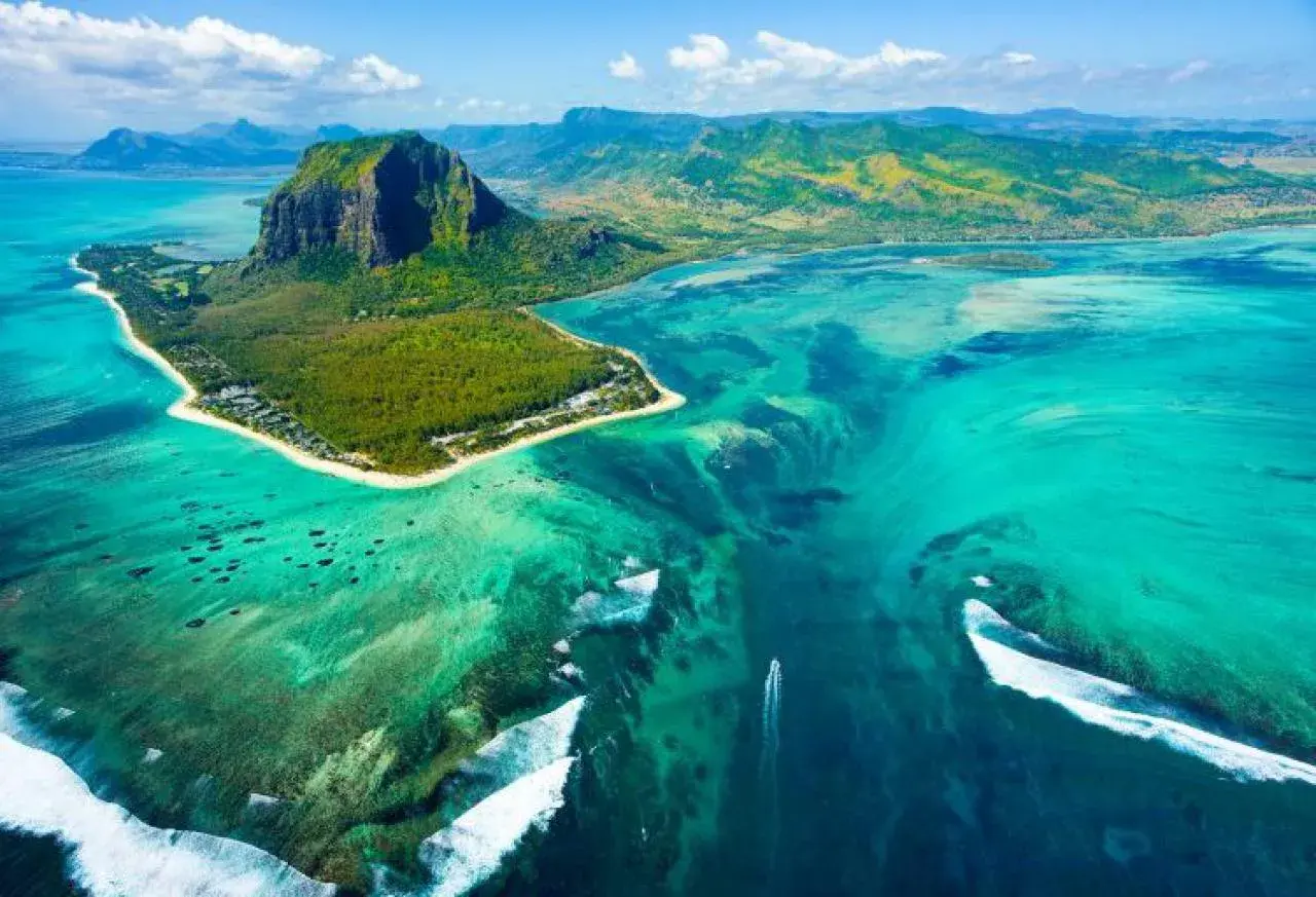 Widok z lotu ptaka na Le Morne Brabant, Mauritius, gdzie leży ta wyspa. Turkusowa woda, rafy koralowe i góra tworzą iluzję podwodnego wodospadu.