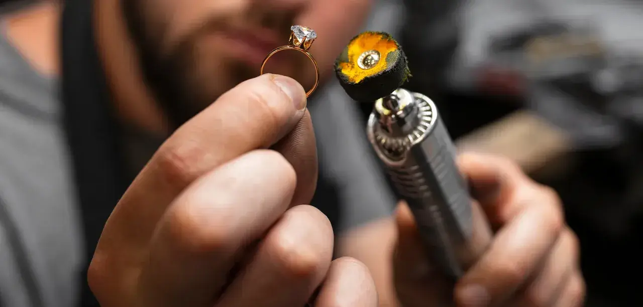 Manos de joyero puliendo un anillo de oro con un diamante. La herramienta de pulido tiene una placa de oro en su extremo.