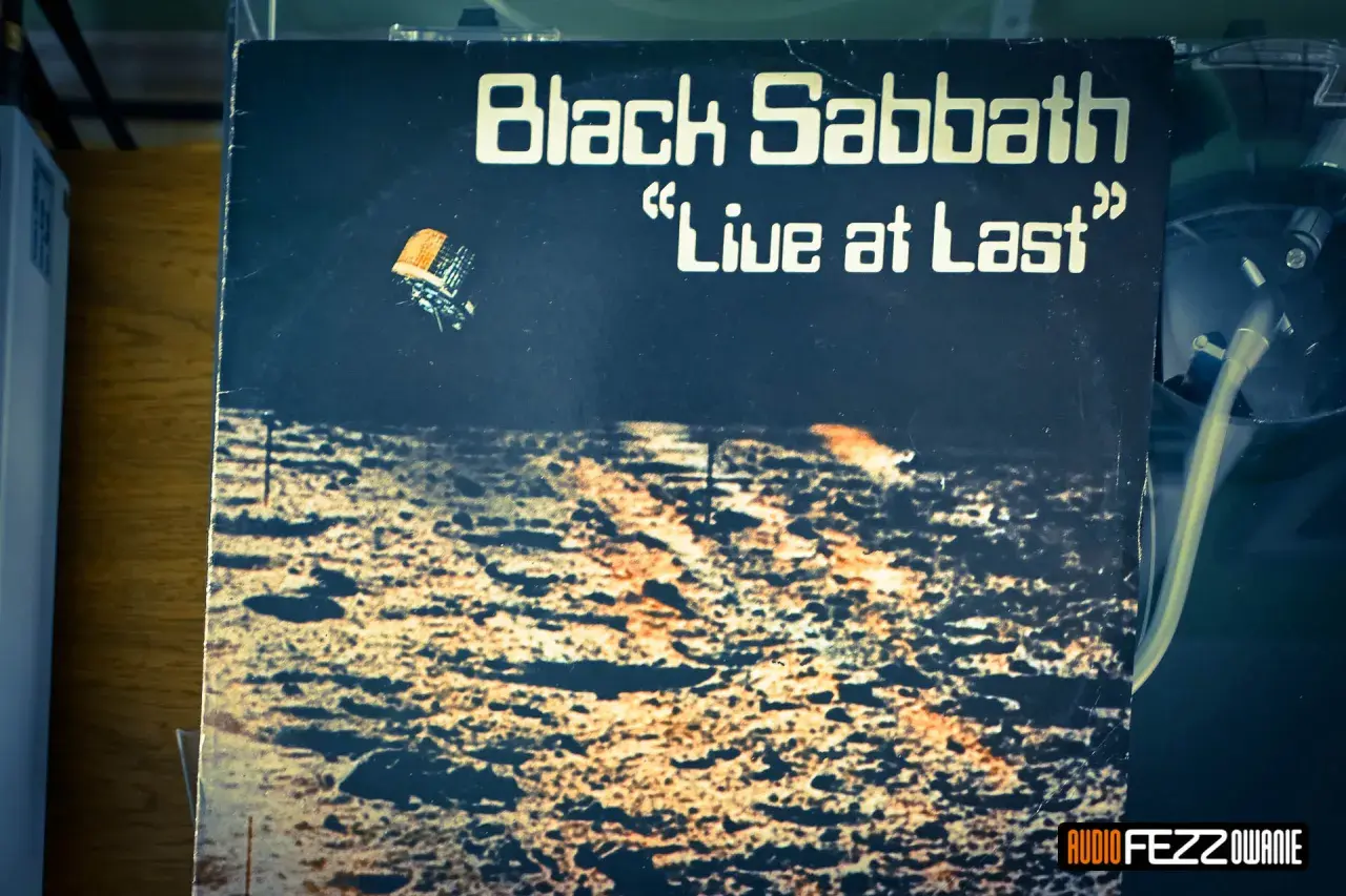 Okładka płyty "Black Sabbath 'Live at Last'". Widok z lotu ptaka na pustynny krajobraz, z małym pojazdem unoszącym się w powietrzu.