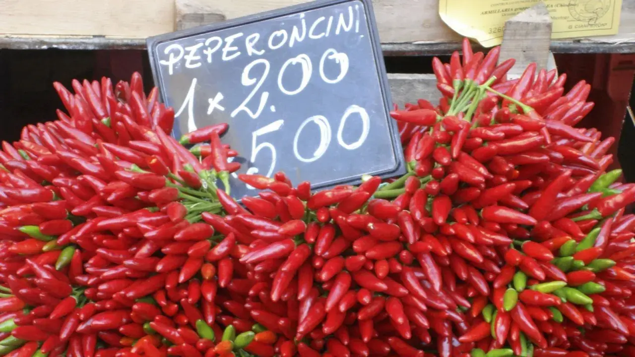 Montón de peperoncini rojos y verdes frescos, con un cartel que indica "Peperoncini 1x2.00 5.00".