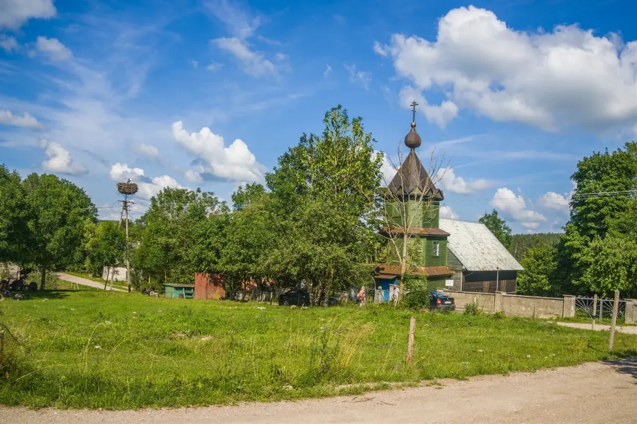 Zielona cerkiew, symbol tradycji starowierców w Polsce, na tle błękitnego nieba z chmurami. Bociany w gnieździe na słupie.