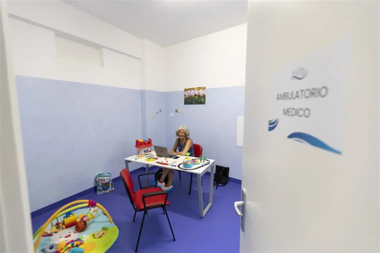 Un ambulatorio medico con una donna al computer, giocattoli e un tappeto gioco. La differenza tra ambulatorio e poliambulatorio è la specializzazione.