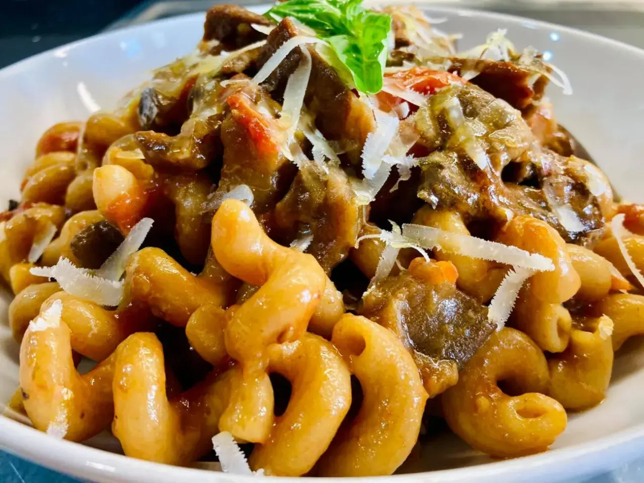 Un piatto invitante di pasta con melanzane, condita con un ricco sugo e scaglie di parmigiano.