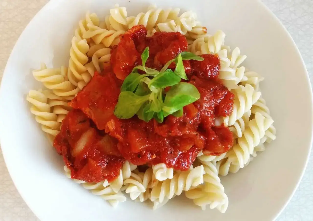 Fusilli con la mejor salsa de tomate italiana, cubierta con una hoja verde fresca.