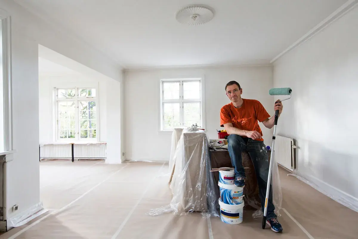 Målare med roller redo att måla bakom elementet i ett rum under renovering.