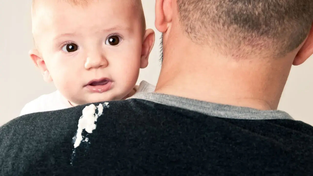 Un neonato di 1 mese ha un rigurgito, lasciando una macchia sul maglione del padre.