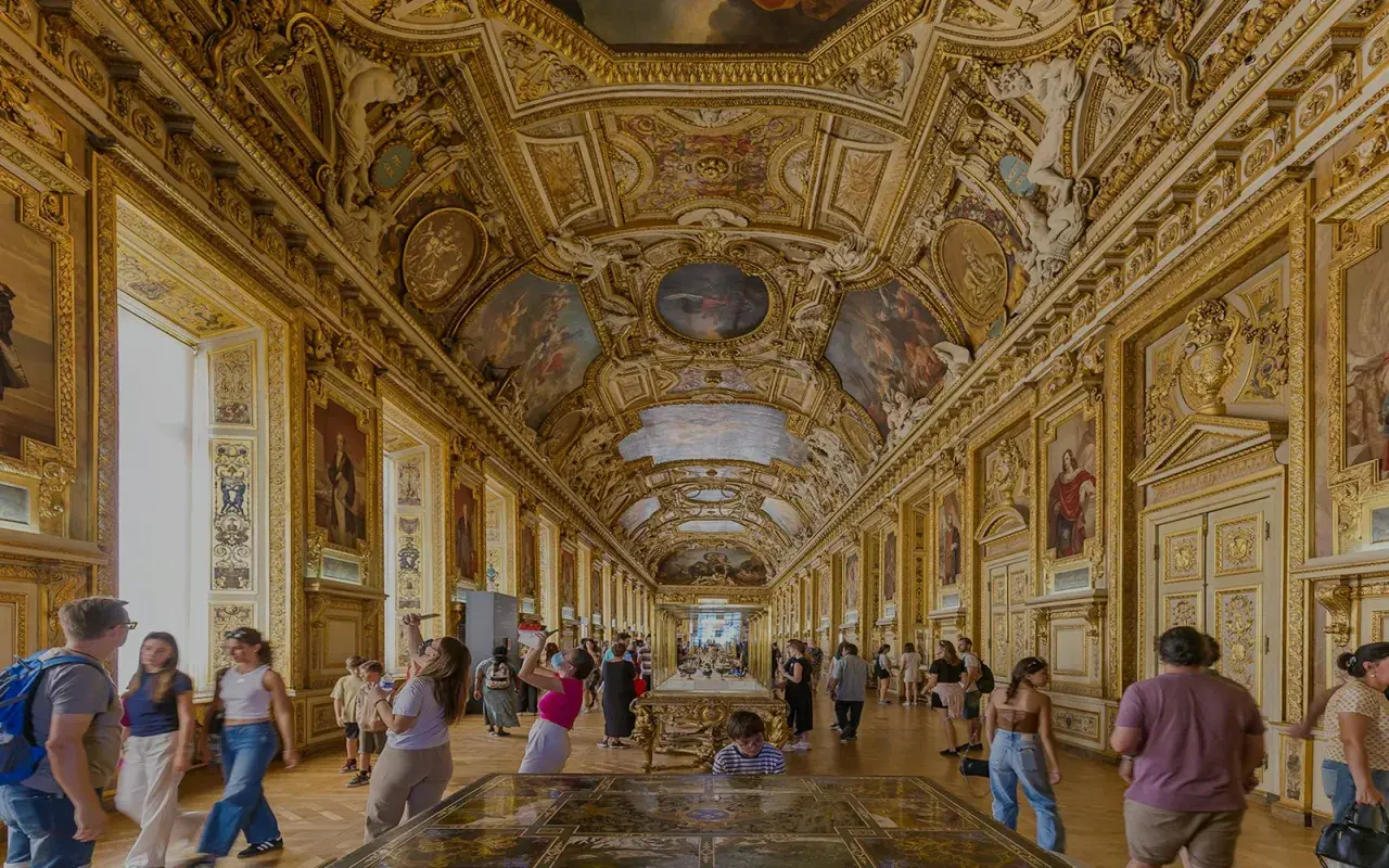 Prunkvolle Deckenmalereien und goldene Verzierungen im Louvre von innen. Besucher bestaunen die Kunstwerke in der langen Galerie.