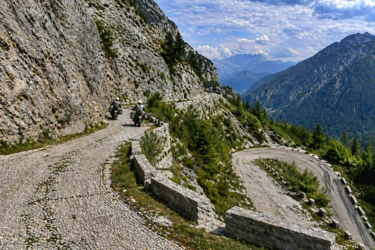 Due motociclisti affrontano tornanti mozzafiato sul passo del Tarvisio, tra rocce imponenti e valli verdi.