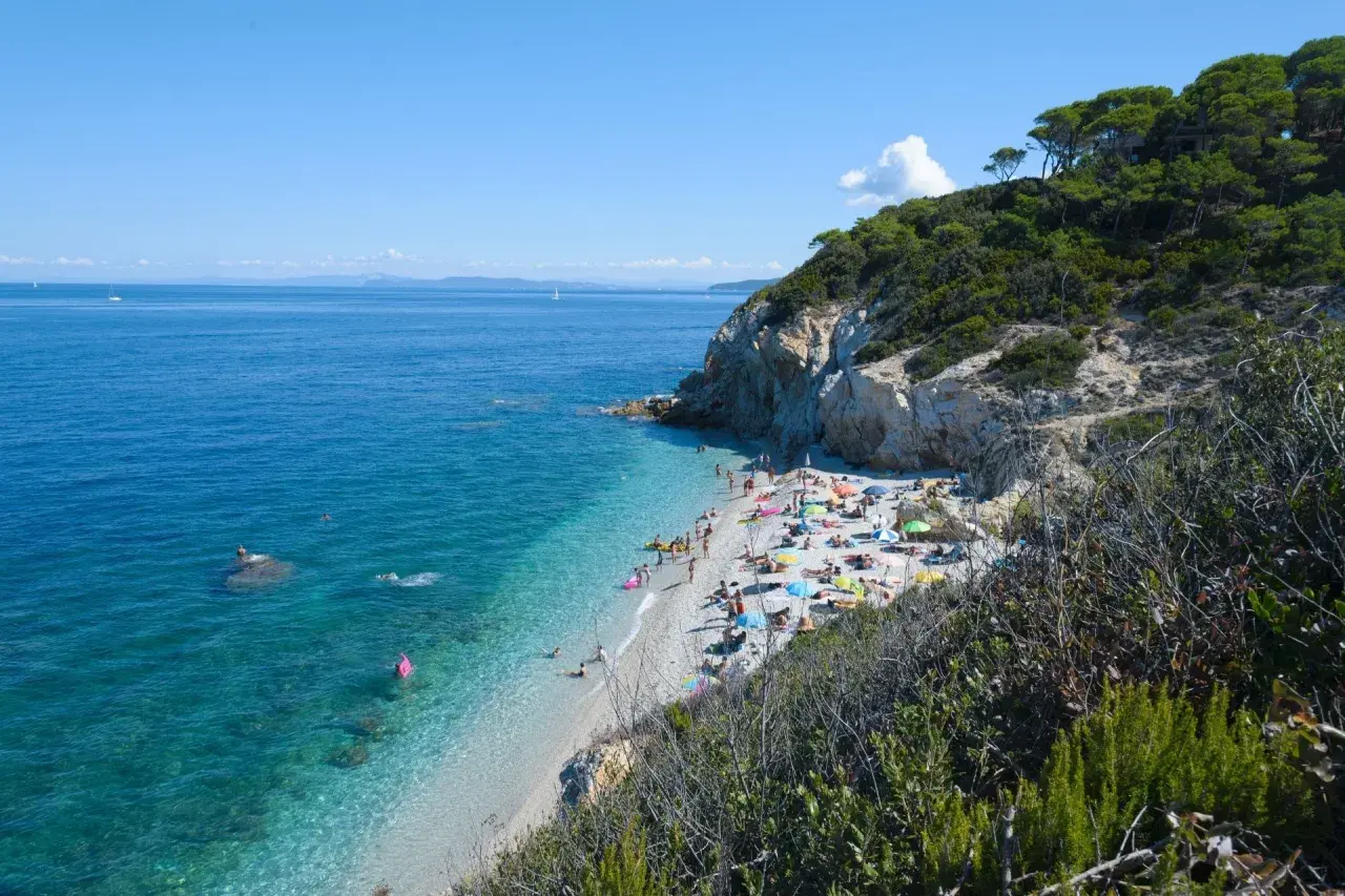 Spiaggia affollata vicino a Campiglia Marittima, con gente che prende il sole e nuota nelle acque cristalline.