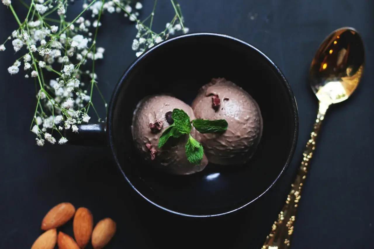Deux boules de glace à la figue, garnies de menthe fraîche, dans un bol noir, avec des amandes et une cuillère dorée.