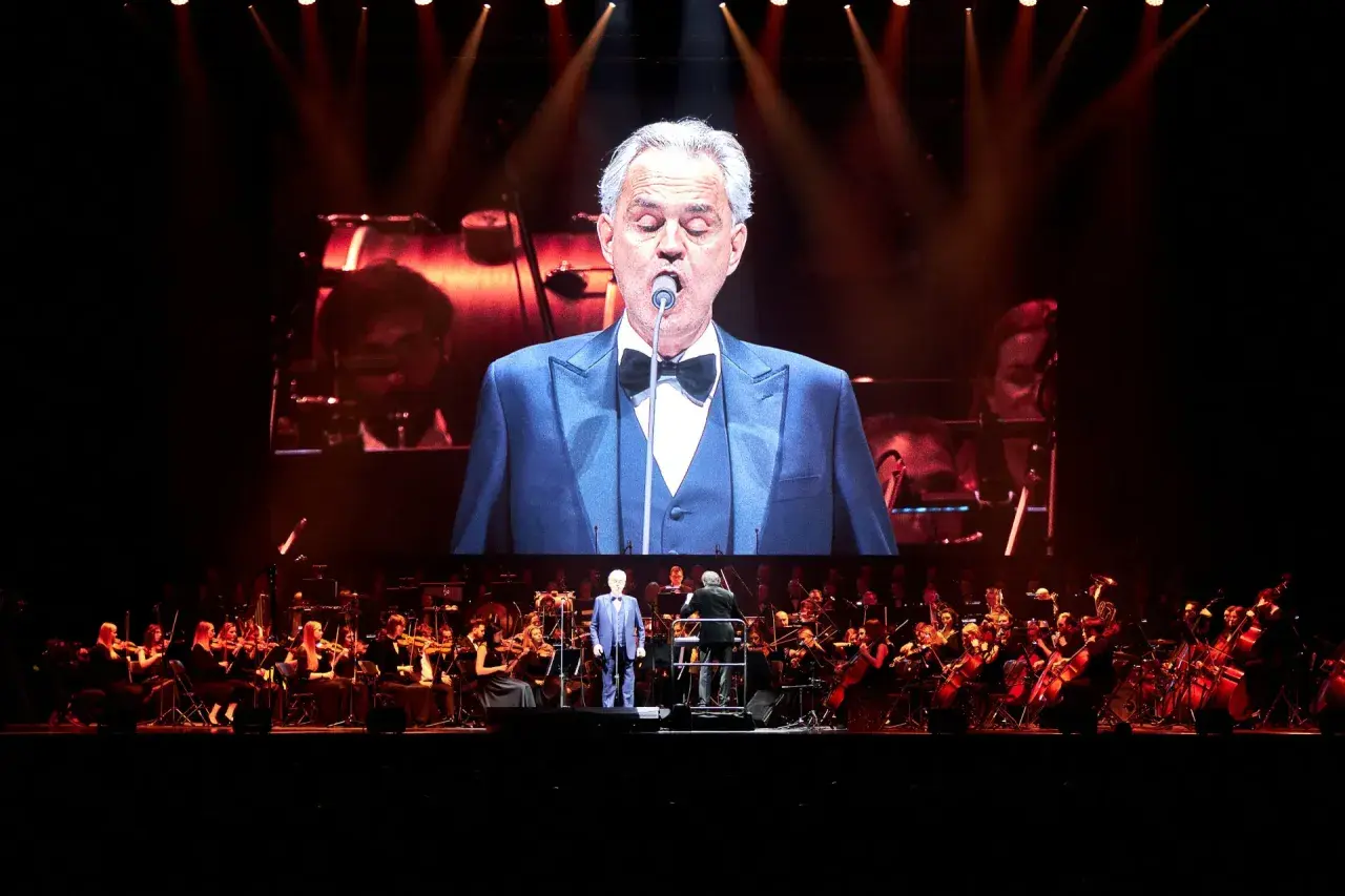 Andrea Bocelli w Gdańsku na koncercie z orkiestrą. Wokalista w garniturze na wielkim ekranie.