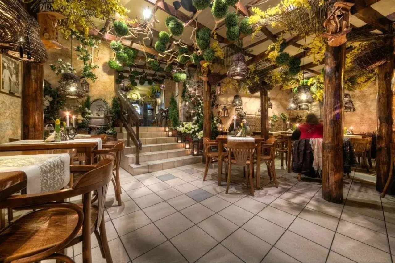 Przytulne wnętrze z drewnianymi meblami i bogatą roślinnością, idealne na romantyczną kolację. Polecane restauracje Katowice.