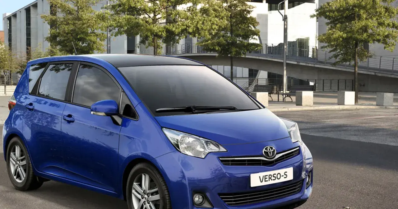 Niebieski Toyota Verso S z czarnym dachem zaparkowany przed nowoczesnym budynkiem.
