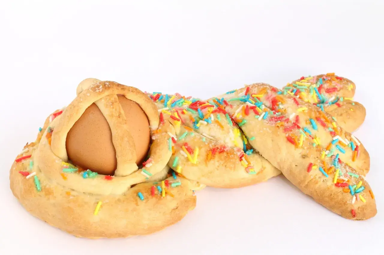 Una cuzzupa intrecciata con un uovo al centro, decorata con zuccherini colorati.
