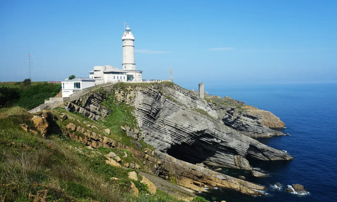 El faro de Cabo Mayor se alza sobre acantilados rocosos, vigilando el azul mar Cantábrico.