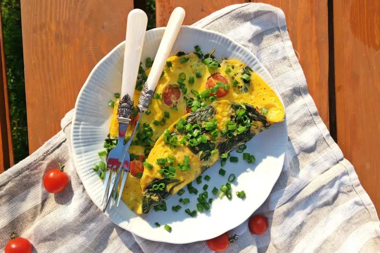 Pyszny omlet ze szpinakiem i pomidorkami, posypany szczypiorkiem, czeka na talerzu. Idealny na letnie śniadanie.