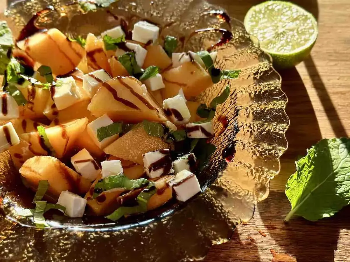 Sałatka z melona, sera feta, mięty i polewy balsamicznej w szklanej misie.