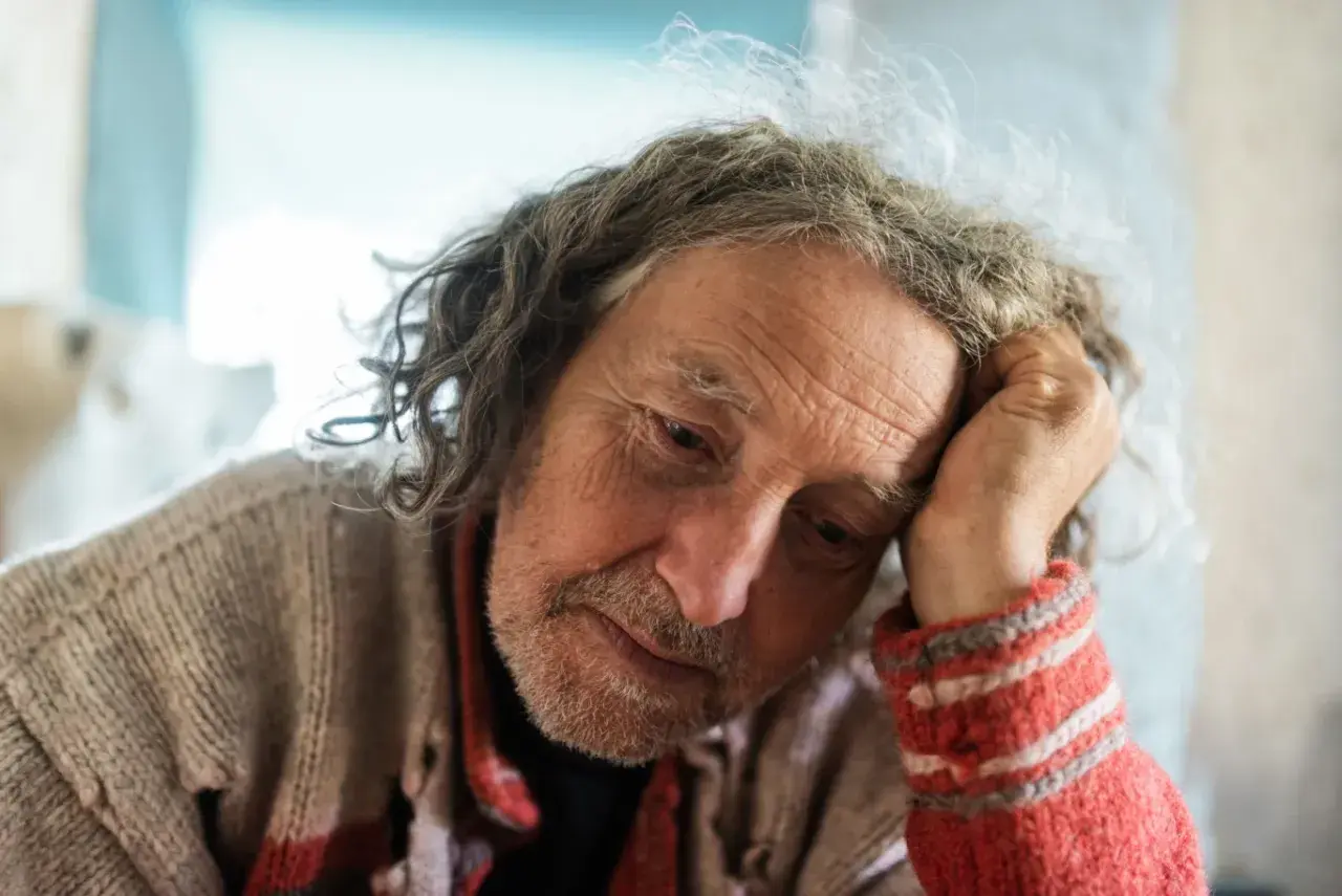 Zamyślony mężczyzna z kręconymi włosami, w swetrze, przypomina postać z opowieści o zespole Diogenesa, szukającego sensu życia.