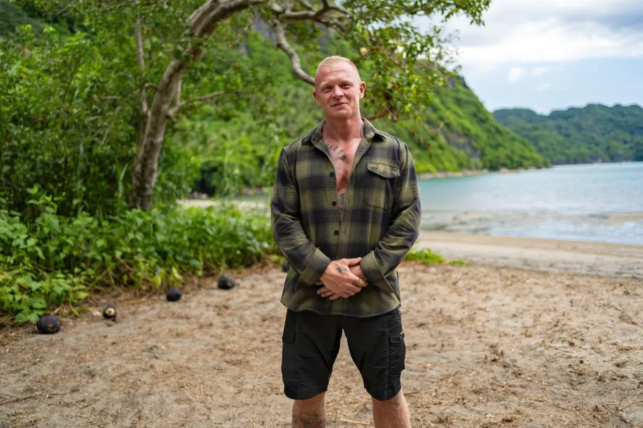 Alexander Strandberg Robinson står på en strand med gröna kullar och vatten i bakgrunden.