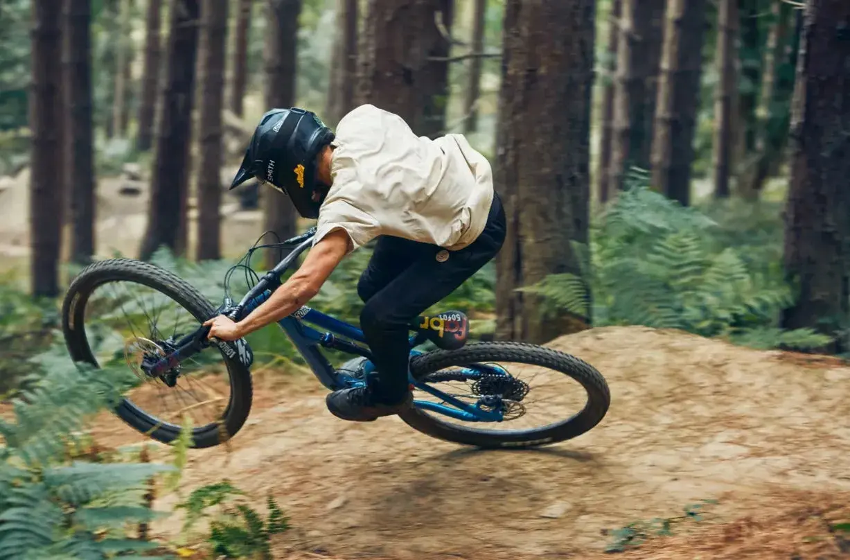 Rider in a forest, mid-air, demonstrating perfect mtb suspension tuning for a smooth landing.