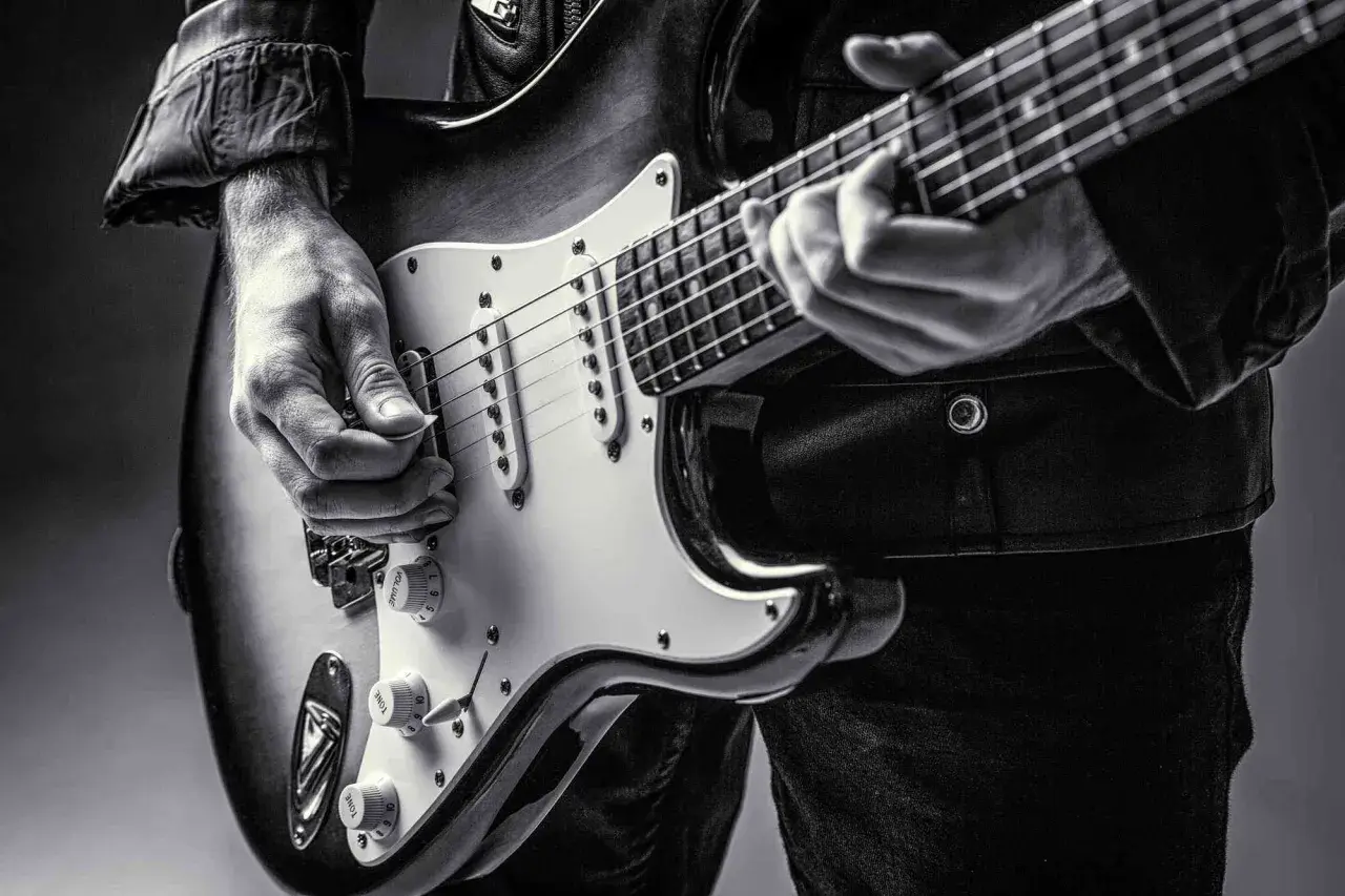 Dłoń gra na gitarze elektrycznej, ukazując klasyczne **marki gitar elektrycznych**.