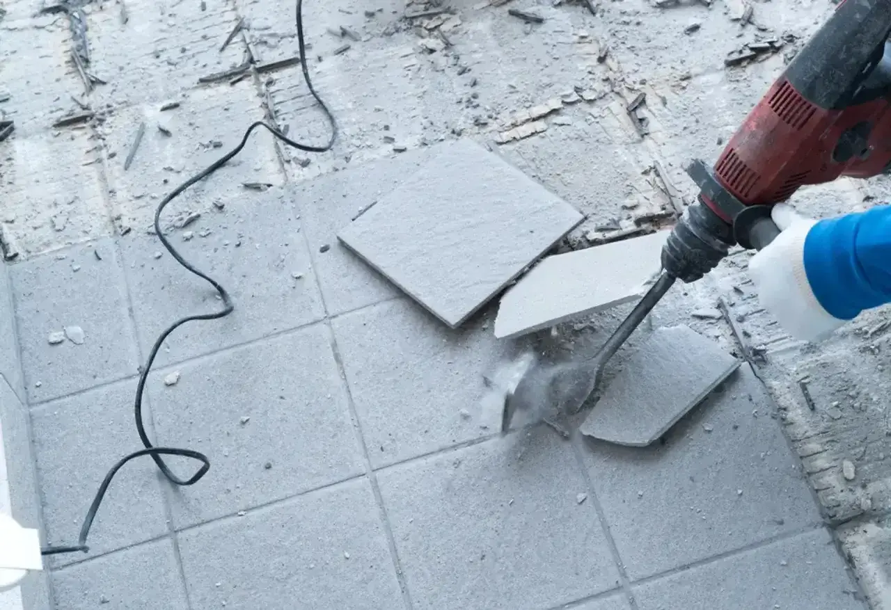 Skuwanie płytek cena: młot udarowy kruszy szare płytki na podłodze, tworząc pył i gruz.