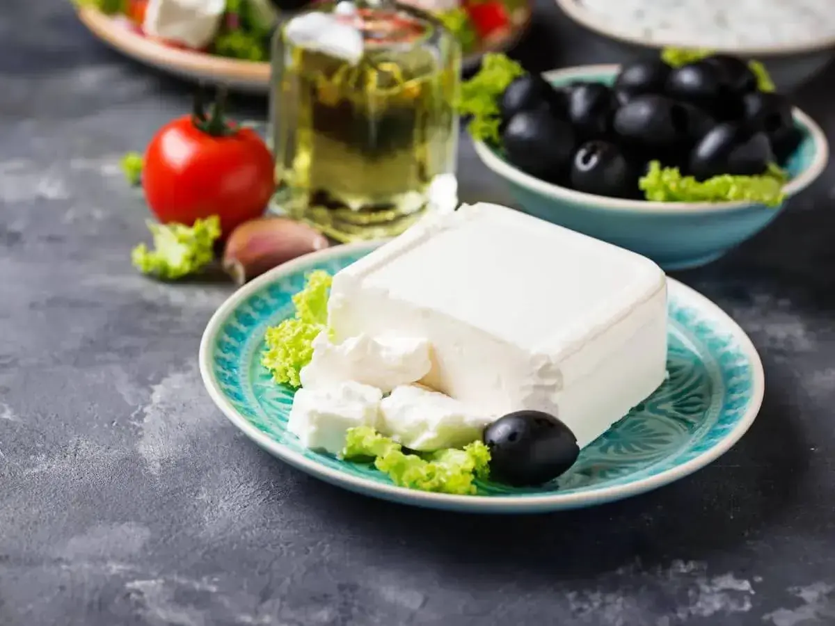 Un blocco di feta su un piatto turchese, con olive, pomodoro e olio d'oliva. La feta proprietà è l'ingrediente principale di questa deliziosa insalata greca.
