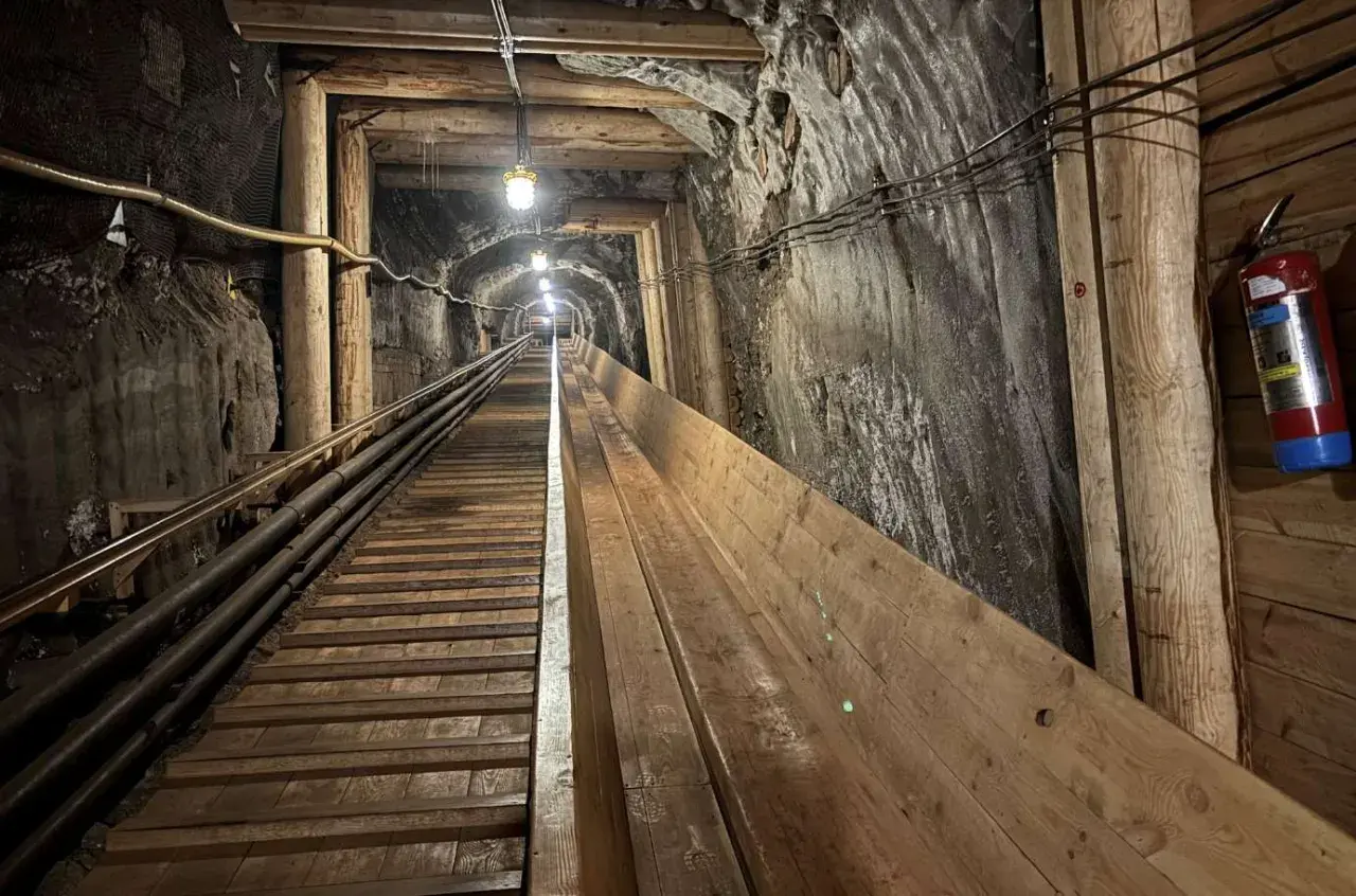 Długi, drewniany tunel w kopalni w Krakowie, oświetlony lampami, prowadzi w głąb ziemi.
