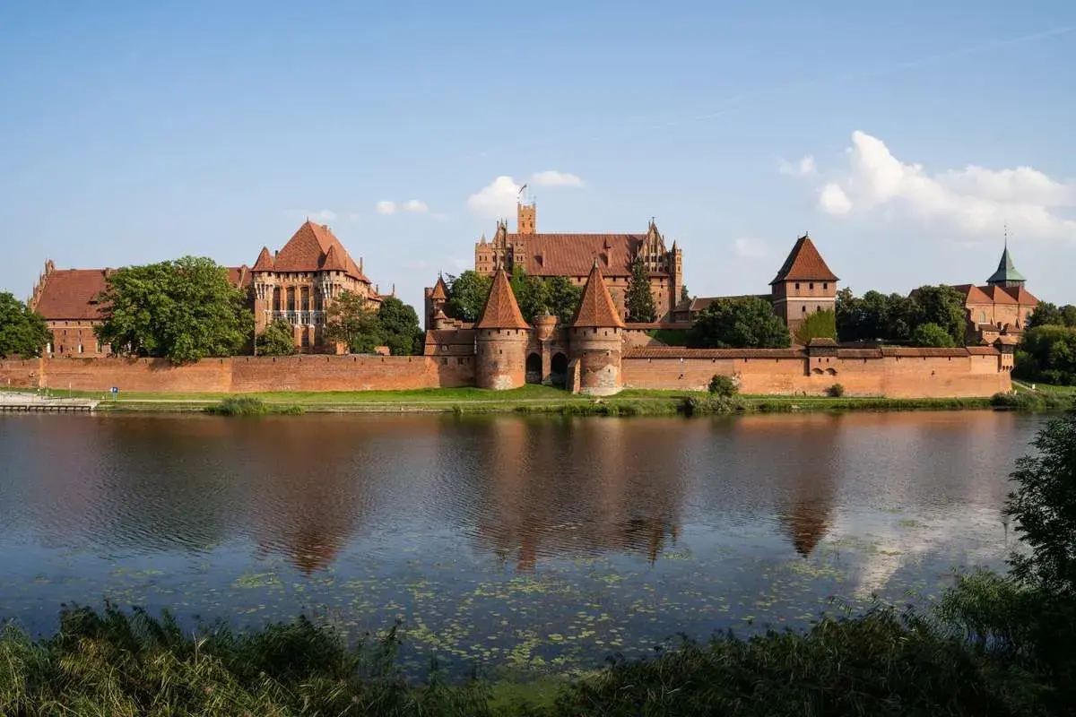 Potężny zamek w Malborku, odbijający się w wodzie. Ciekawostki o jego historii i architekturze budzą podziw.